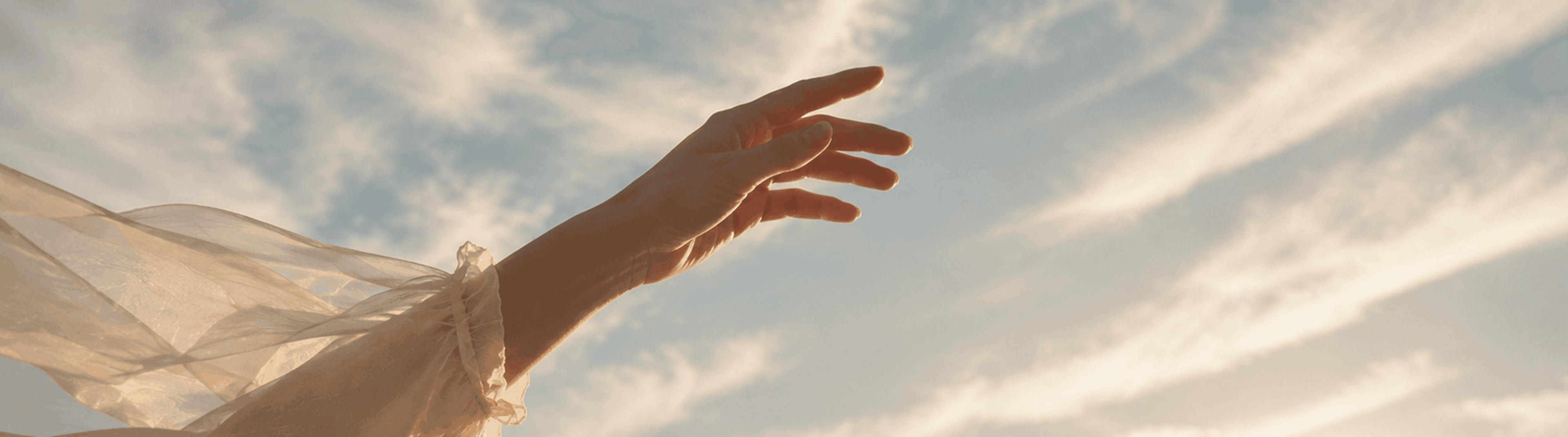 Photo - A hand reaching toward the sky against white clouds.