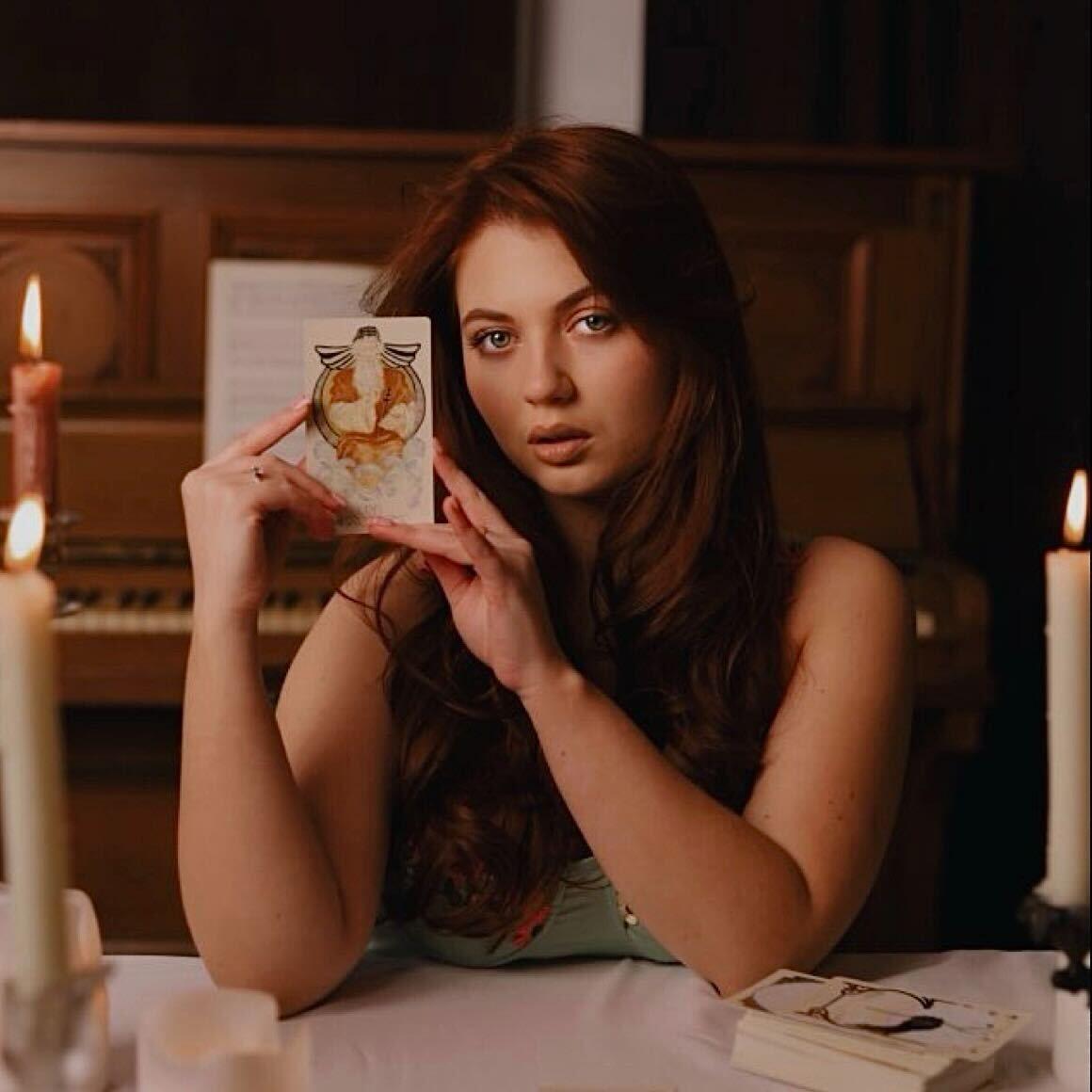 Spiritueel adviseur die bij kaarslicht een tarotkaart omhooghoudt, op de profielpagina Photo - Spiritueel adviseur die bij kaarslicht een tarotkaart omhooghoudt, op de profielpagina